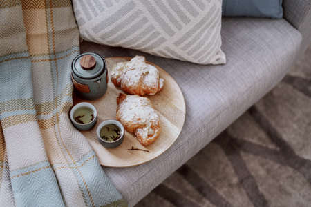 High angle of fresh homemade croissants and chinese tea in small cups. Breakfast tray with pastry and traditional beverage on wooden plate in living room. Enjoy dessert and drinks at home, top viewの写真素材