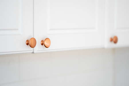 Concept of renovation, replacement detail. Selective focus at round copper door handles on white cabinet in classic style. Close up of new knob on kitchen furniture, blurred copy space backgroundの写真素材