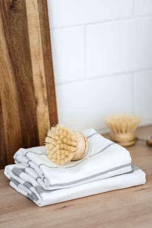 Vertical shot of dishwashing brush with eco friendly material on clean towels against wooden cutting boards at kitchen. Sustainability life. Domestic, housework and home cleaning conceptsの写真素材