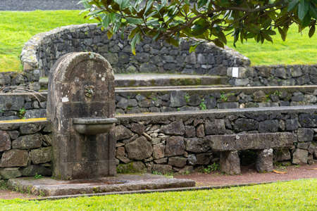 Drinking fountain with faucet and sink for washing hands in public park. Parkland with stone bench and recreational zone in city garden. Concept of ennoblement of municipal territoriesの写真素材