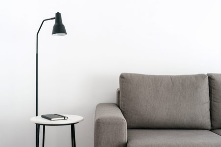 Notepad and lamp on nightstand near sofa in white styled room. Minimalist and contemporary interior...