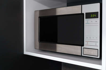 Closed microwave oven with timer standing on shelf. modern kitchen appliances. Cooking food at home. defrosting equipment. modern technologyの写真素材