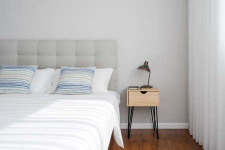Side view of bedroom interior design with clean white lines. Minimalistic home decorations. Bedside table with lamp. natural light in the morning. Cozy apartmentの写真素材