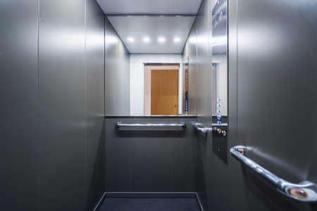 Stainless steel elevator cabin interior with mirror. Modern passenger lift with convenient control panel in building. transport concept. Accessible environment for disabled peopleの写真素材