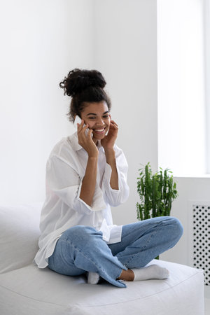 Side view of happy and pretty afro american lady talking to phone at home and smiling. Communication...