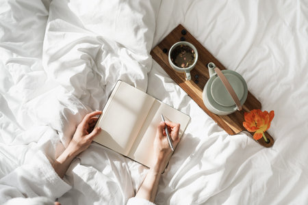 High above view of person making notes using notebook and pen, kettle and morning coffee, romantic mood, cozy bedroom interior design, home decor, flat layの写真素材