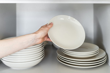 Cropped view of person's hand stacking white ceramic dishes after washing. home comfort. household...