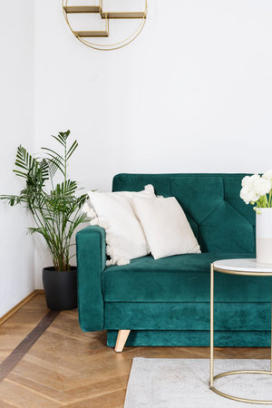 Boho design of living room with emerald velours couch, white cushions, coffee table with flower in...