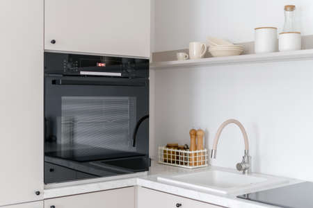 Side view of contemporary black oven, sink and kitchenware. White wood furniture with appliances and decor. bakery concept. Cozy place for cookingの写真素材