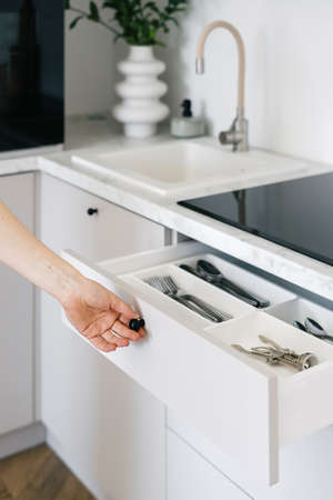 Cropped view of woman open white cutlery drawer in a modern apartment. Housewife holding clean shiny silverware in box with separate sections. Concept organization of space at kitchenの写真素材