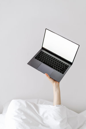 Person's hand holding laptop when lying in bed, busy people, gadgets addiction, modern technology,...