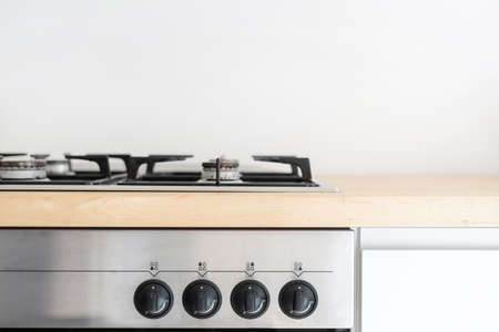 stainless steel gas cooker built in wooden countertop and electric oven with black control knob switch at contemporary kitchenの写真素材