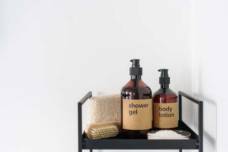 closeup of shower gel and body lotion in plastic bottles, wooden nail brush, soft bath sponge and sea salt in bowl on black metal shelf in home bathroom, copy spaceの写真素材