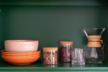 order in kitchen and storage concept, kitchenware, ceramic plates, bowl, glass, jar with beans and...