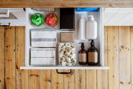 top view of opened drawer with towels, washing sponge, detergent bottles and dishwashing tablets in plastic box in modern kitchen cabinet in apartment, storage conceptの写真素材