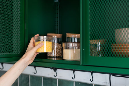 storage grains and beans in jar on shelf in metal green cabinet at kitchen and female hand taking...