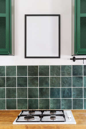 built in white gas cooker appliance, wooden countertop surface, green tile and mockup picture in black frame on wall at kitchen, contemporary interior of apartmentの写真素材