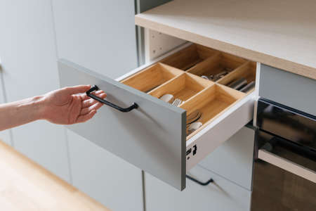 person hand open wooden drawer with metal handle or wood section for keeping silverware, spoons, forks, knife and cutlery in gray cupboard at contemporary kitchenの写真素材