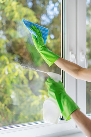 cleaning service concept. female hands in green protective gloves hold spray bottle with detergent...