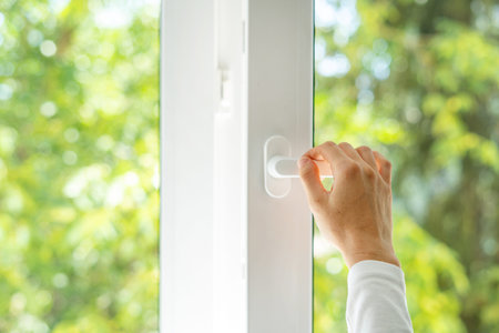 closeup of female hand open plastic pvc window with white frame and handle installed at house, view...