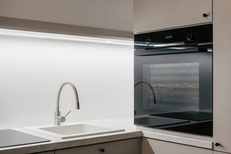 Side view of black built-in oven and beige sink in modern kitchen interior design. Contemporary beige furniture. luxury apartment after renovationの素材 [FY310191361434]