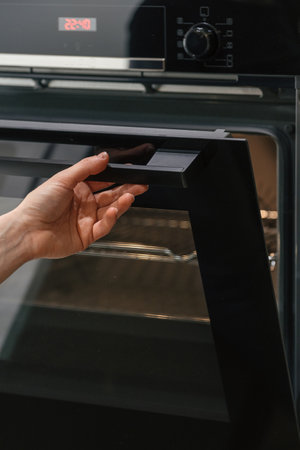 POV of woman hand opening glass door in empty electric oven with light inside. Housewife preparing homemade food using new built-in appliance at home. Household equipment in modern apartmentの写真素材
