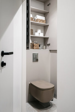 Storage closet with paper rolls, clean towels, hygienic accessory in bathroom over built in toilet bowl installed on wall. Opened doors on cupboard with household items. restroom interiorの写真素材