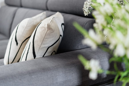 detail of interior in living room, view on cushions on comfort couch through blurred blossom...