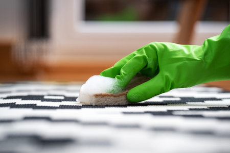 housemaid hand in green rubber glove wash floor carpet with soap foam and sponge in living room with...