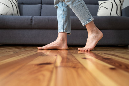 cropped shot of female legs walk barefoot on wooden warm floor near couch in living room at home, heating conceptの写真素材