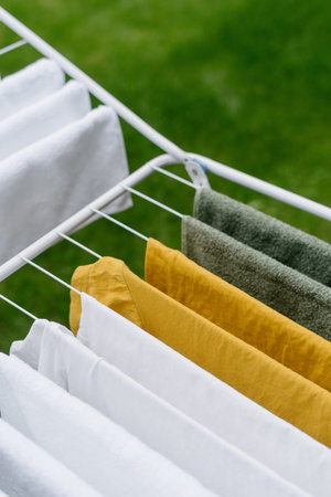 closeup of wet fresh textile apparel hanging on metal portable drying rack in backyard after laundry...