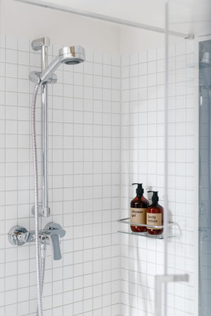 Vertical view of shower cabin with white tile on wall in hotel room. Dispenser bottle with gel and...