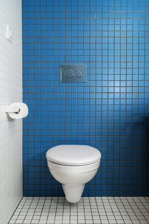 Installed concealed water cistern in restroom. White built in toilet bowl with closed cover hanging...