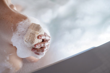 High angle view of woman hand using bath sponge, washing soft skin, making bodycare and home spa procedure. Beauty treatment, peeling, exfoliation, self and body care conceptsの写真素材
