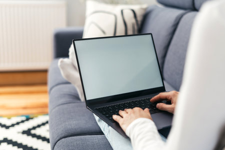 cropped shot of female hands hold notebook pc with mockup screen, typing keyboard and communicate online on couch in living roomの写真素材