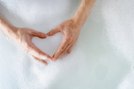 Beauty routine and self care procedure concepts. Top view of woman taking bath, hold hands in hot bubble water, making heart shape and showing love gestureの写真素材