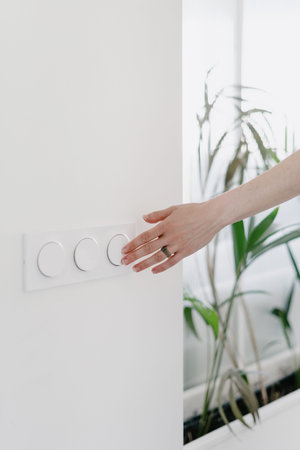 cropped shot of female hand press on plastic round switch button at modern apartment with light...