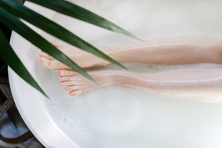 Cropped shot of female legs. Top view of woman lying in bathroom tub with warm water and bubbles....