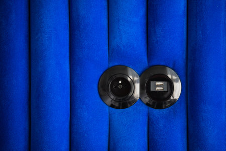 closeup of round plastic power outlet and usb connector on velor upholstered wall panel in room, electric supplyの写真素材