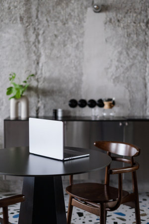 pc notebook with gray cover, round table and brown wood chair on blurred kitchen background in...
