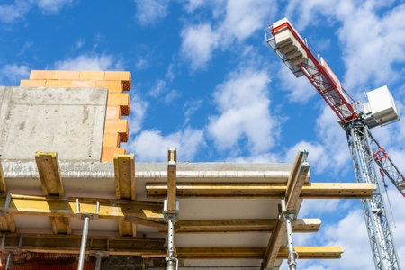 construction site. Residential house, real estate concepts. Low angle view of crane lifts cargo on the rooftop of brick building. Metal scaffolding with wooden blocks supports the ceiling in the apartmentの素材 [FY310194174235]