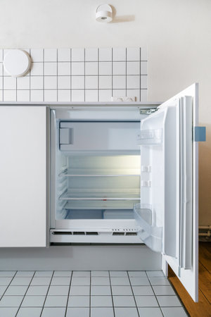 empty refrigerator with open door and shelves inside, compact modern freezer in kitchen interior with white furniture, tile on wall and floor, household applianceの写真素材