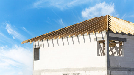 view of unfinished building from concrete blocks and rooftop with wooden truss planks outdoors on blue sky backgroundの写真素材