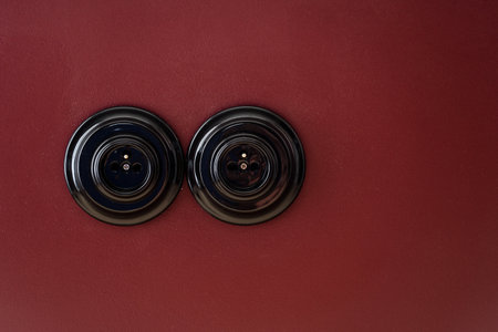 Close up view of old fashioned electrical socket in black frames isolated on red wall. Renovated apartment with power supply in vintage style and copy space backgroundの写真素材