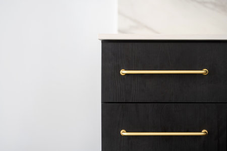 closeup of dark wooden closed drawers with golden handles on white wall background with copy space, detail in design of furniture in interiorの写真素材