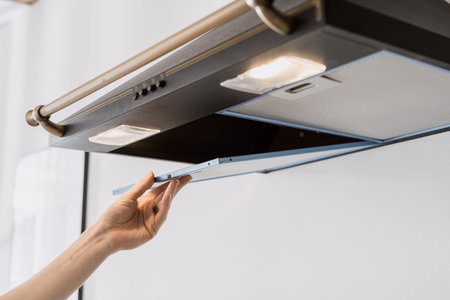 cropped shot of black metal hood extractor and person hand taking aluminum mesh filter on white wall...