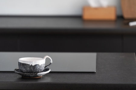 closeup of cup and saucer with pattern on kitchen island countertop near induction glass ceramic hob on blurred background at modern apartmentの写真素材