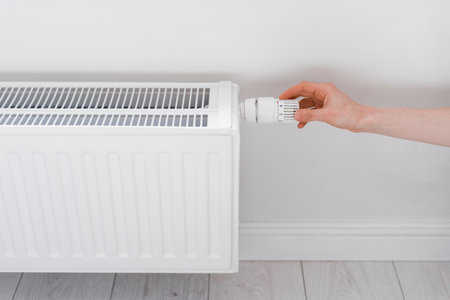 female hand adjusting radiator temperature in living room, comfort heating at home, energy efficient, economy conceptの写真素材