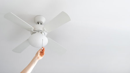 cropped shot of female hand pull switch of ceiling fan with lamp on white background with copy space, room cooling and ventilation conceptの写真素材