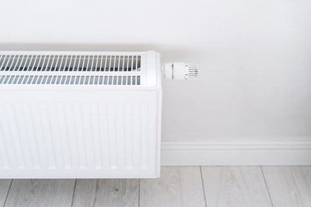 metal heating radiator with thermostatic valve for regulation and controlling temperature in house, mounted on white wall, energy efficient conceptの写真素材